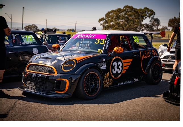 Number 33 track Mini in pit lane, black with orange livery, roll cage visible